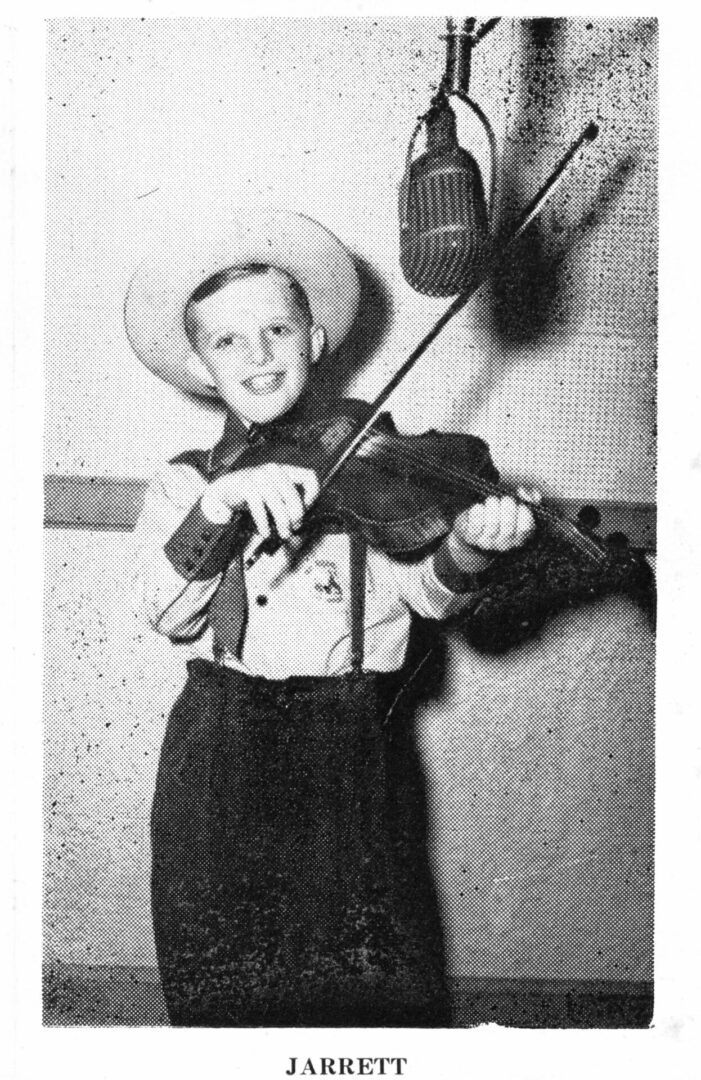 A young boy in cowboy attire holding a violin.