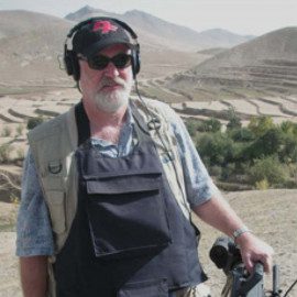 A man in black shirt holding camera near hills.