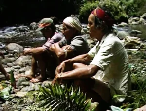 Three people sitting on rocks near a river.