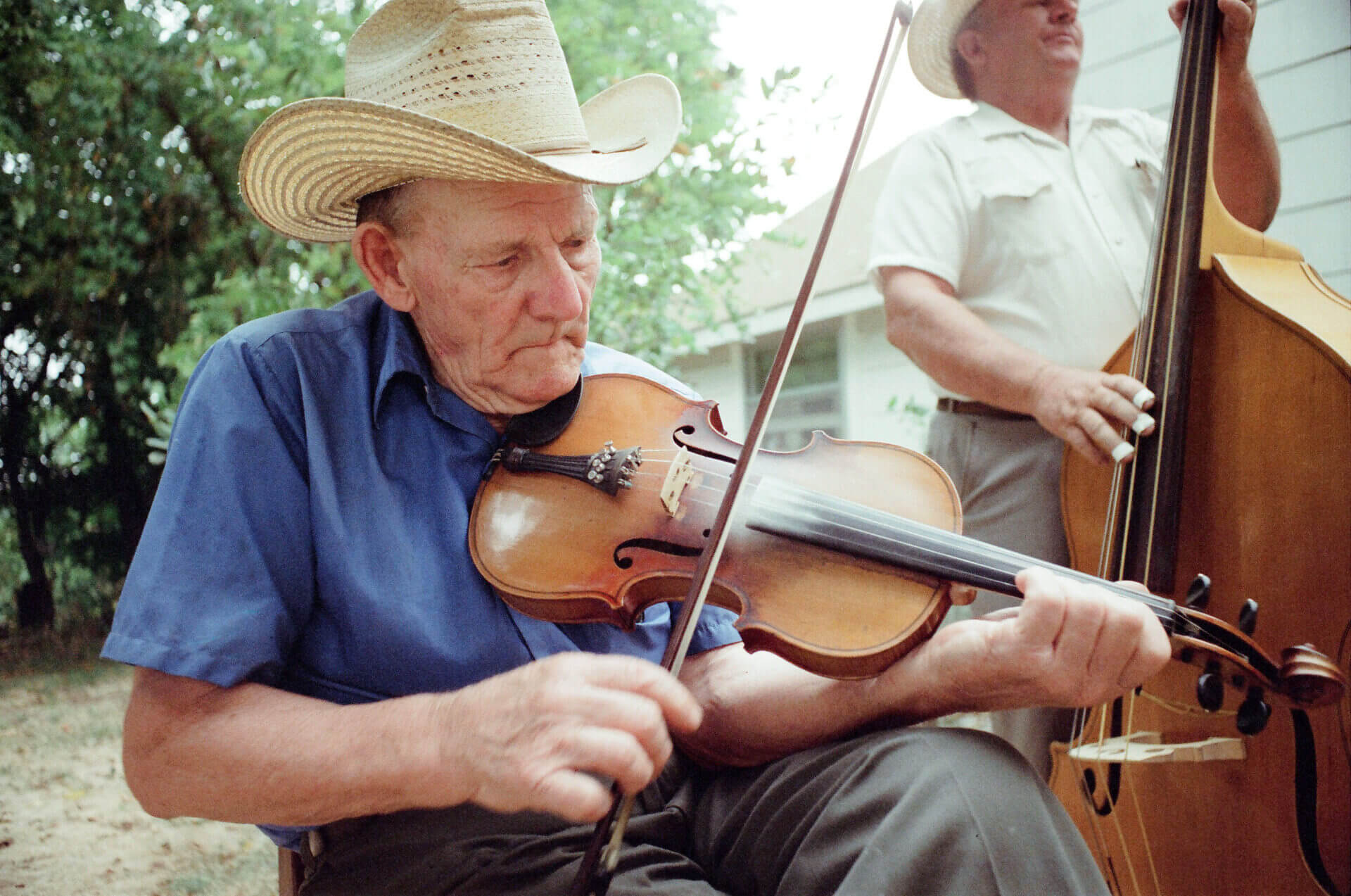 A man in cowboy hat playing violin while sitting on chair.